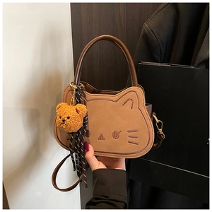 Dettaglio di una borsa marrone a forma di gatto con ricamo e un ciondolo a forma di orsetto
