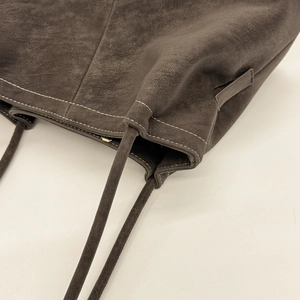 Detail of dark brown matte leather tote bag featuring contrast white stitching
