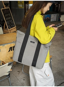 Close-up of light grey tote bag with wide black handles and front pocket in natural light