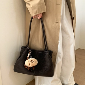 Detail view of dark brown matte tote bag with white stitching and plush paw charm accessory