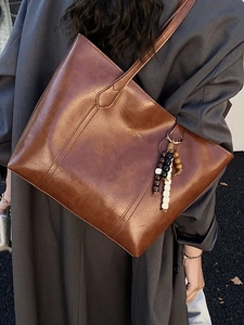 Retro brown leather tote bag with beaded charm worn by a model in a long coat