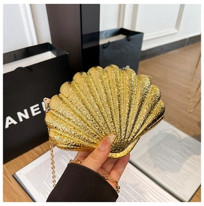 Detail of a golden shell evening bag featuring a textured wave surface and elegant chain