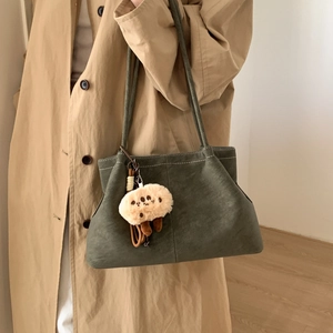 Detail of vintage matte green tote bag with white stitching and plush charm on model