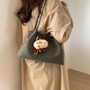 Detail view of dark green matte shoulder bag with cookie plush charm and white contrast stitching