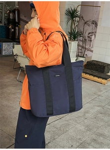 Navy blue large capacity tote bag with wide straps shown on male model in orange jacket