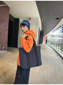 Detail view of large dark blue tote bag with wide black straps on outdoor model