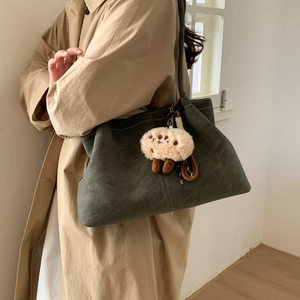 Olive green suede tote bag detail with plush charm and stitching on khaki coat