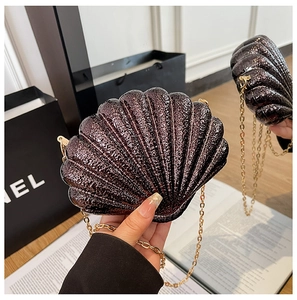 Detail of shell-shaped evening clutch with glossy metallic texture and golden chain strap