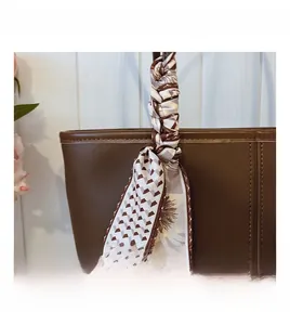 Detail of brown leather tote bag handle featuring a decorative geometric silk scarf accent