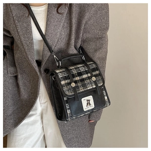 Detail of tweed checkered crossbody bag with bear patch and leather strap on model