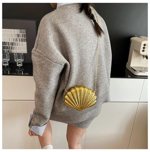 Detailed back view of a golden shell-shaped chain bag worn by a model in a cafe