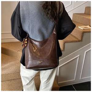 Detail der braunen Leder-Beuteltasche mit Perlenquaste und goldener Beschriftung