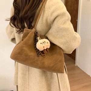 Brown frosted leather shoulder bag with white stitching and plush paw charm on model