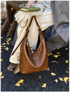 Braune Leder-Hobotasche mit Holzperlenanhänger auf herbstlichem Ginkgo-Hintergrund
