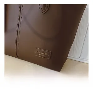 Detailed macro view of brown leather tote bag stitching and brand embossed patch