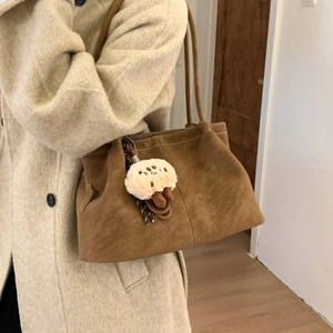 Detail of a brown matte suede tote bag with a cute plush charm on a shoulder strap