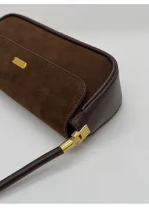 Détail du sac en daim marron foncé montrant la boucle dorée mate et les coutures