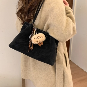 Close-up of black matte suede shoulder bag with white stitching and cute plush pendant