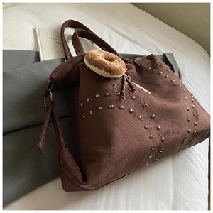 Detail der dunkelbraunen Wildleder-Tote-Bag mit Nieten und Plüsch-Donut-Anhänger am Bett