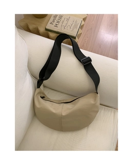 Close-up of beige nylon crescent bag with black adjustable strap on a white sofa