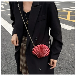 Macro detail of red shell-shaped crossbody bag with metallic finish and gold chain strap