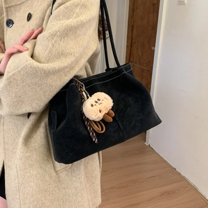 Detail of black matte suede shoulder bag with contrast stitching and plush animal charm