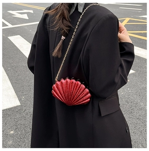 Red glitter shell-shaped hard shell bag worn with a chic golden chain shoulder strap