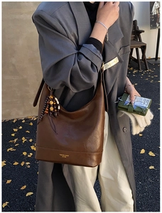 Detail der braunen Vintage-Wachsleder-Beuteltasche mit Boho-Perlenquaste und Goldlogo