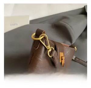 Detailed close-up of the golden metal lobster clasp and D-ring on dark brown leather bag