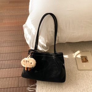 Detail of black leather tote bag with white contrast stitching and plush charm