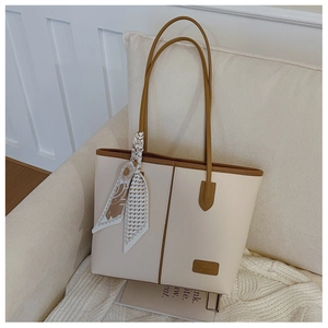 Détail d'un grand sac fourre-tout beige avec bordure marron et foulard sur un canapé