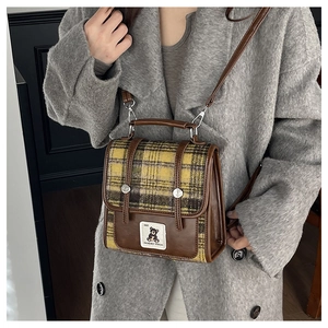 Détail d'un mini sac à dos à carreaux vintage avec garniture en cuir sur un manteau gris