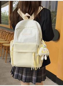 Detail of cream backpack with star print, yellow tassels, and plush monster pendant