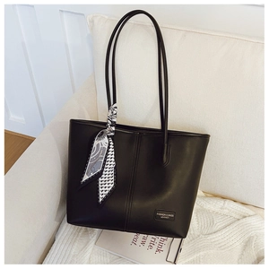 Détail d'un cabas noir en cuir mat avec une écharpe décorative et un badge de mode