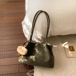 Close-up of olive green matte shoulder bag with plush pendant and white contrast stitching