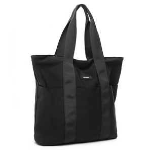 Detail of minimalist black tote bag featuring wide shoulder straps and brand logo patch