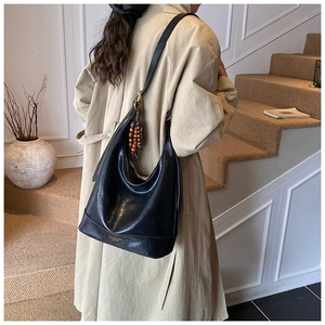 Detail einer großen schwarzen Hobo-Tasche aus Leder mit dekorativem Holzperlen-Anhänger am Riemen