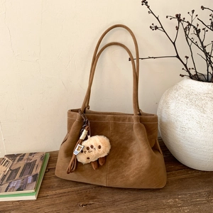 Detail of a brown matte suede tote bag with a plush sheep charm on a rustic wooden table