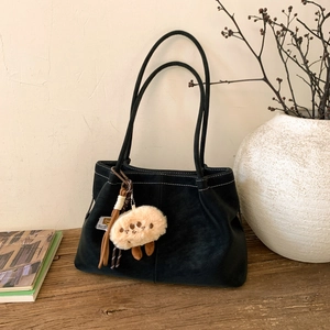 Detail of black matte tote bag with white contrast stitching and plush beige charm