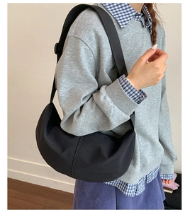 Detail of a large black nylon dumpling crossbody bag worn by a model in casual style