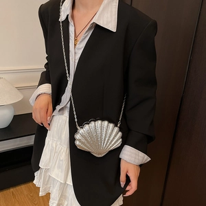 Silver shell-shaped evening bag with metallic finish and delicate chain strap on model