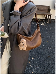 Detail of a large brown faux leather hobo bag with a cute plush bear charm on the strap