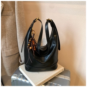 Detail der schwarzen Hobo-Tasche aus Leder mit goldenem Logo und Perlen-Anhänger auf Koffer