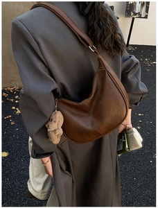 Detailed back view of a brown crescent tote bag with a cute plush dog charm on street