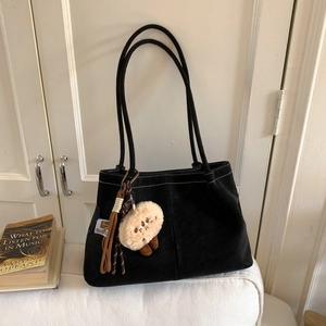 Detail of black matte tote bag with contrast stitching and plush mascot charm