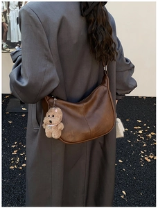 Close-up of a brown leather crescent tote bag featuring detailed stitching and a cute plush charm