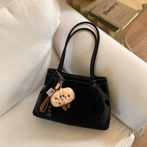 Detail of black suede tote bag with white contrast stitching and plush biscuit charm