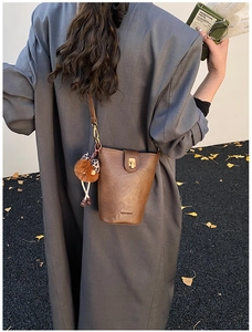 Brown leather bucket bag detail with leopard bow charm on model in autumn grey wool coat