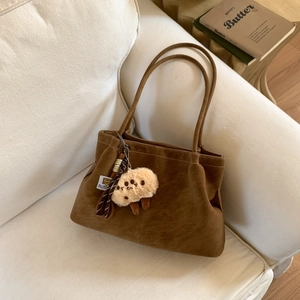 Brown suede tote bag detail with tassel and plush charm on a cozy cream sofa
