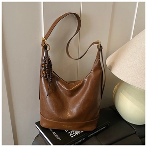 Detail einer braunen Leder-Hobo-Tasche mit Holzperlenquaste und goldener Schnalle auf Büchern